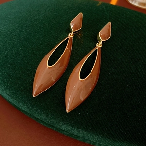 Detail of caramel enamel teardrop earrings on green velvet with golden metallic finish