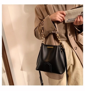 Elegant black leather bucket bag with gold chain handle shown on a model in a tan blazer