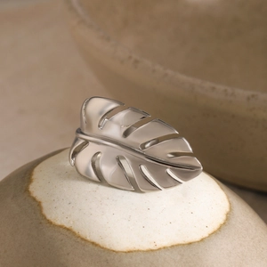 Macro detail of silver monstera leaf ring on ceramic pottery with polished metal texture