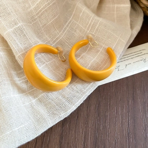 Macro detail of bright yellow acrylic C-shaped hoop earrings on beige linen texture