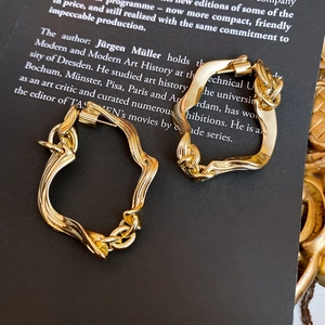 Detail of gold irregular twisted chain earrings displayed on a vintage dark book