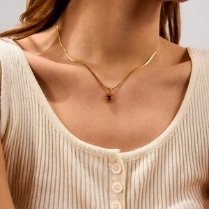 Dettaglio di una collana a catena serpente dorata con ciondolo a cuore rosso sul modello