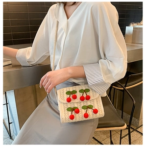 Detailed straw shoulder bag with plush cherry accents and slim strap on a model