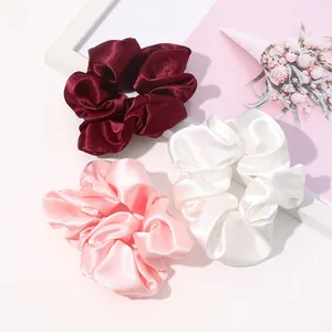 Detailed close-up of three silk satin hair scrunchies in burgundy, white, and pink colors