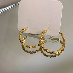 Detailed close-up of golden geometric textured hoop earrings with faceted design
