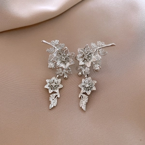 Macro detail of silver floral drop earrings with hollow petals on champagne satin cloth