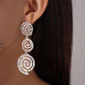 Détail de boucles d'oreilles pendantes spirales argentées texturées portées par un mannequin