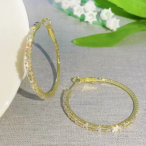 Luxurious gold hoop earrings with baguette-cut zircons leaning on white ceramic