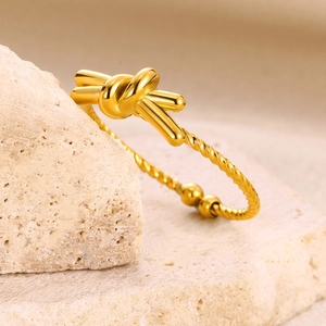 Macro detail of a gold-toned knot cuff bracelet featuring twisted rope texture on stone