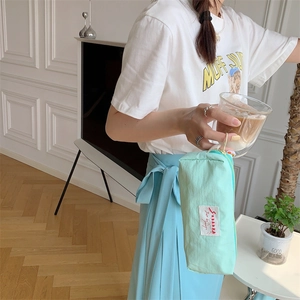 Close-up of a light blue fabric pencil case held by a model in a minimalist setting