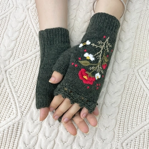 Detailed embroidery of red flowers on dark green knitted fingerless gloves for winter