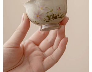 Macro shot of ceramic tea cup with hand-painted pink daisy flowers and green leaves