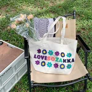 Detail of embroidered floral canvas tote bag with LOVE SOZAKKA text in outdoor picnic setting