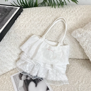 Dettaglio di balze in pizzo bianco a strati e ricami floreali su una borsa di cotone