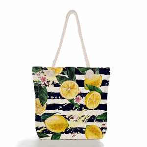 Detail of nautical rope handles and vibrant lemon prints on a striped canvas beach tote bag