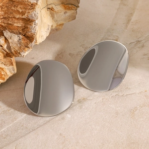 Macro detail of polished silver concave geometric stud earrings on a marble surface