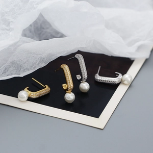Detail of C-shaped pearl earrings in gold and silver finish with sparkling micro-crystals