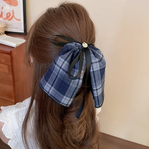 Detail of a large blue-grey plaid bow hair clip worn on long wavy hair with a retro style