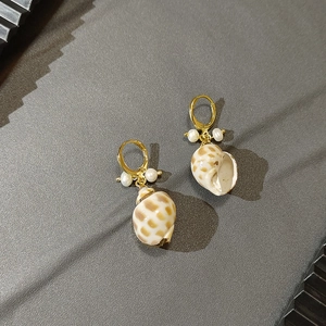 Detailed macro view of golden shell earrings with natural pearl and mother-of-pearl