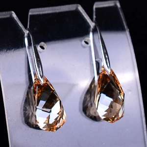 Close-up of champagne teardrop crystal earrings with faceted cut on a clear stand