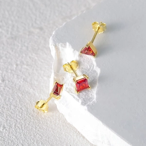 Macro detail of S925 silver gold-plated earring set with red stones on a stone base