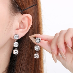 Close-up of dangling cat-eye stone earrings with square tiers and silver tassels