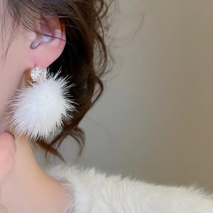 Gros plan sur une boucle d'oreille pompon blanc avec clou en zircon brillant