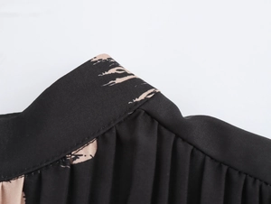 Close-up of pleated black chiffon fabric with abstract beige floral print and neat stitching