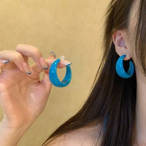Close-up of blue acrylic C-shaped geometric hoop earrings worn on a model's ear