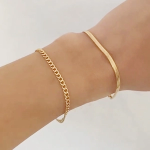 Détail d'un ensemble de bracelets chaîne serpent et gourmette dorés portés au poignet