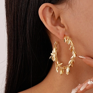 Detailed view of large gold hoop earrings with metallic leaf charms on female model