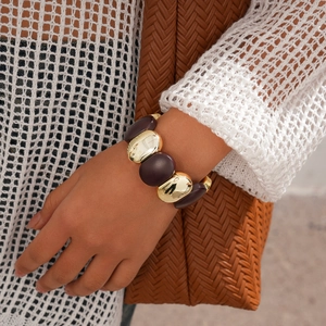 Détail d'un large bracelet en or et acrylique ambré porté au poignet avec un sac tissé