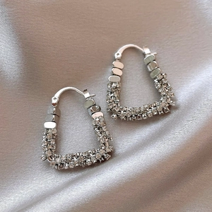 Dettaglio di orecchini a triangolo color argento con pavé di strass su tessuto di seta