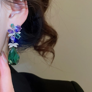 Detail view of luxurious silver needle zircon flower earrings with a green water drop gem.