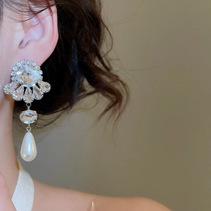 Detail view of flower-shaped silver stud earring with diamond accents and drop pearl on model