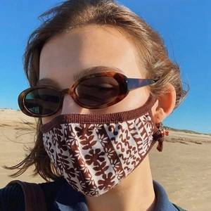 Detail of vintage floral fabric face mask with brown ribbed edges worn by a model at beach