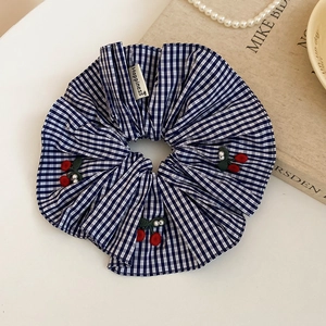 Détail d'un chouchou à carreaux bleus avec broderie cerise et perles blanches décor