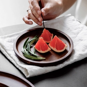 Round dark brown wooden tray with fresh fruit slices and rosemary on white linen