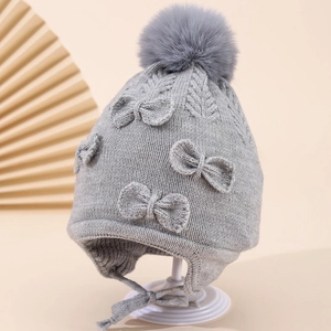 Close-up of grey knit winter hat for girls with fluffy faux fur pompom and side bow