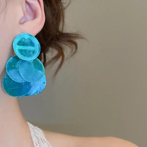 Macro shot of layered teal round sequins earrings worn on a model for vacation style