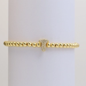 Macro detail of a gold beaded stretch bracelet with a pavé-set letter T charm