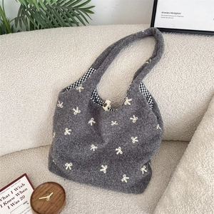 Grey plush tote bag with embroidered bows and gingham lining on a minimalist sofa
