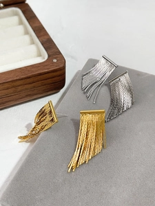 Close-up of gold and silver tassel earrings on a grey velvet tray with wooden box