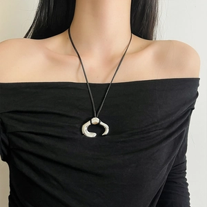 Close-up of sculptural silver C-shaped flower pendant with black cord on neck