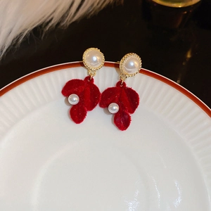 Macro detail of red flocked leaf earrings with pearl accents on a white ceramic plate