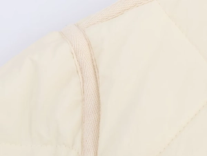 Detailed macro view of off-white quilted jacket fabric with decorative woven trim