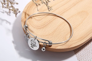 Silver adjustable stainless steel bracelet with cartoon charm on a wooden tray