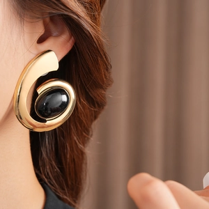 Close-up of vintage gold oval spiral earrings with black stone inlay on a model