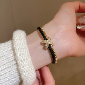 Gros plan d'un bracelet double rang en cuir tressé et chaîne dorée avec breloque X en zircon