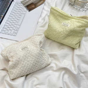 Detail of soft popcorn texture cosmetic bags in cream and pale yellow on a white bed sheet